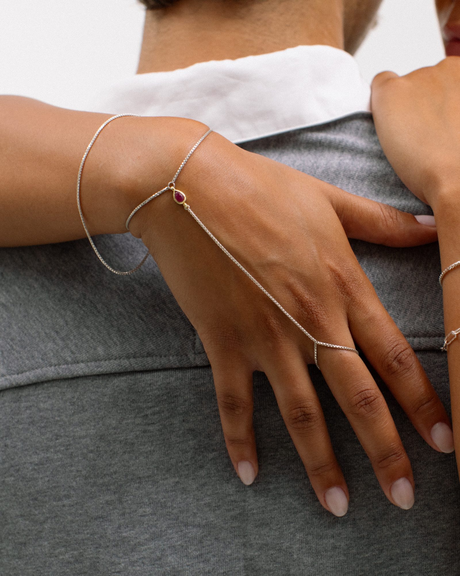 Hand chain prateada com pedra, num abraço